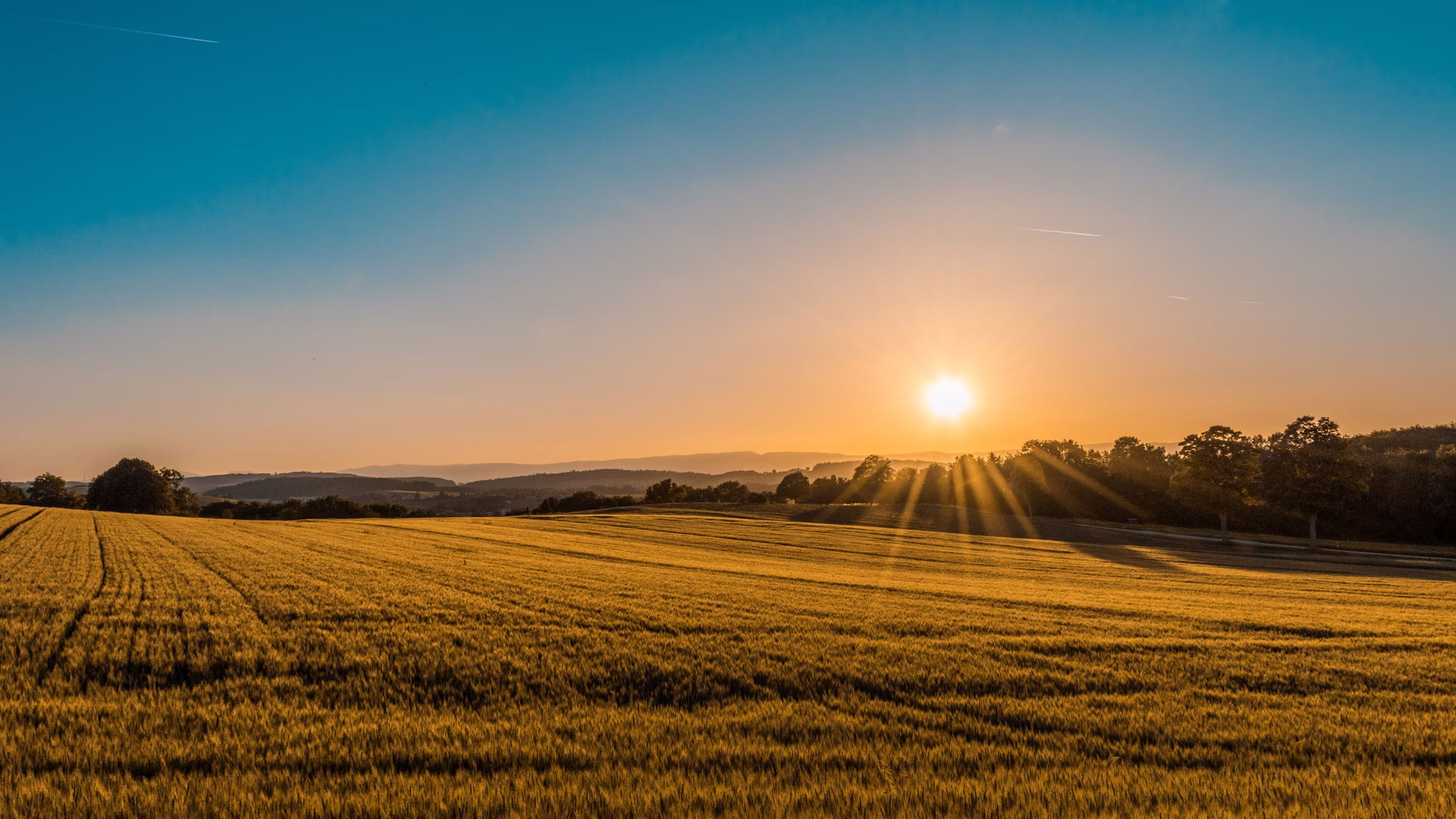 Golden hour over rolling Southeast farmland with sun cresting distant ridges